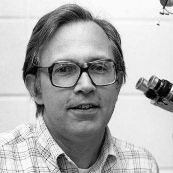 B&W photo of Prof Anderson in glasses and button-down next to a microscope