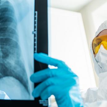 Medical worker in full protective gear examines a chest X-ray