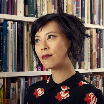 Prof. Sianne Ngai stands next to a bookshelf and looks away from the camera