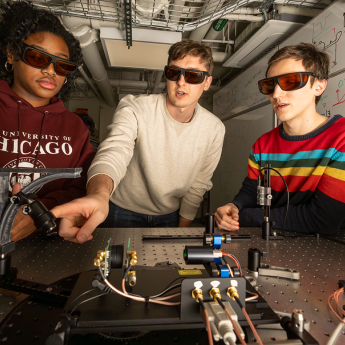 Three people wearing goggles interact with scientific equipment.