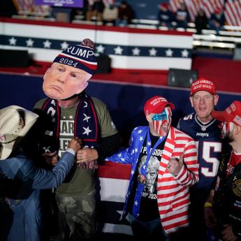 Several men in MAGA apparel stand near a stage