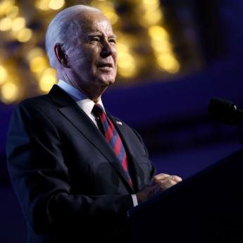 President Joe Biden stands at a podium, backlit by warm yellow lights