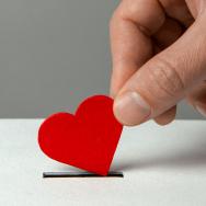 A hand holding a paper heart, inserting it into a coin slot