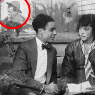 Black and white still from the film The Trooper of Troop K. A man and woman sit on a front stoop looking at each other. The woman is holding a letter. In the left-hand corner is a superimposed scene of a man in a military hat talking to a woman.