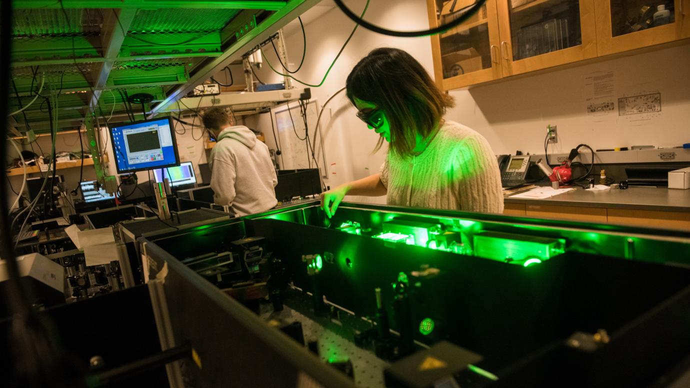 Scientist works at a table wearing protective glasses with green laser light 