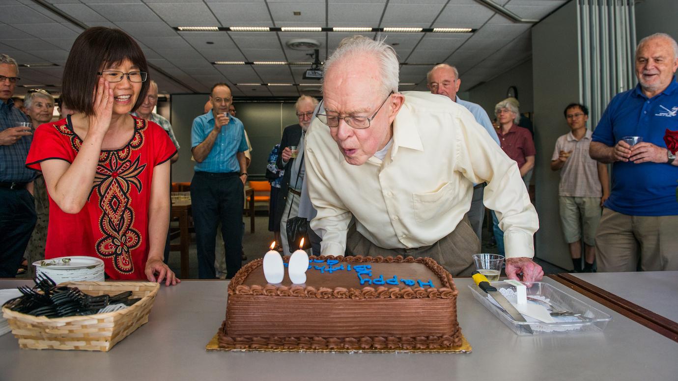 Eugene Parker blows out candles on a cake surrounded by UChicago colleagues