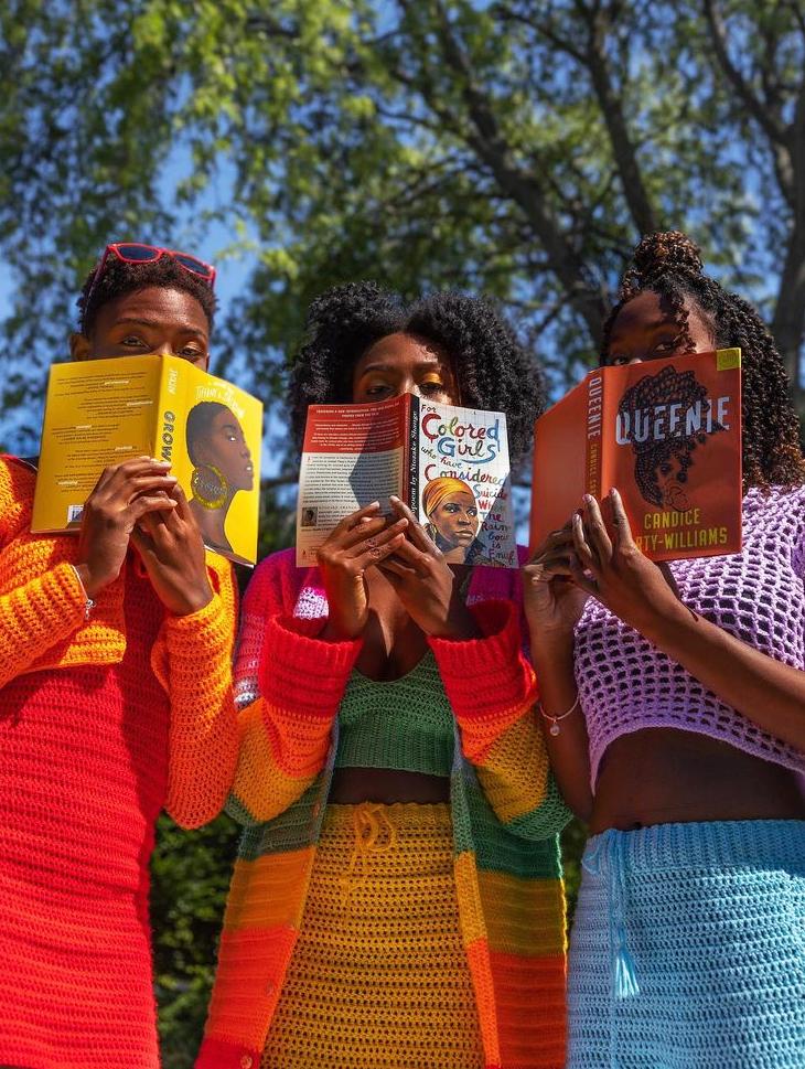 Dinah Clottey (center) with sisters Halle and Cherith, holding books over their faces and wearing brightly colored clothes