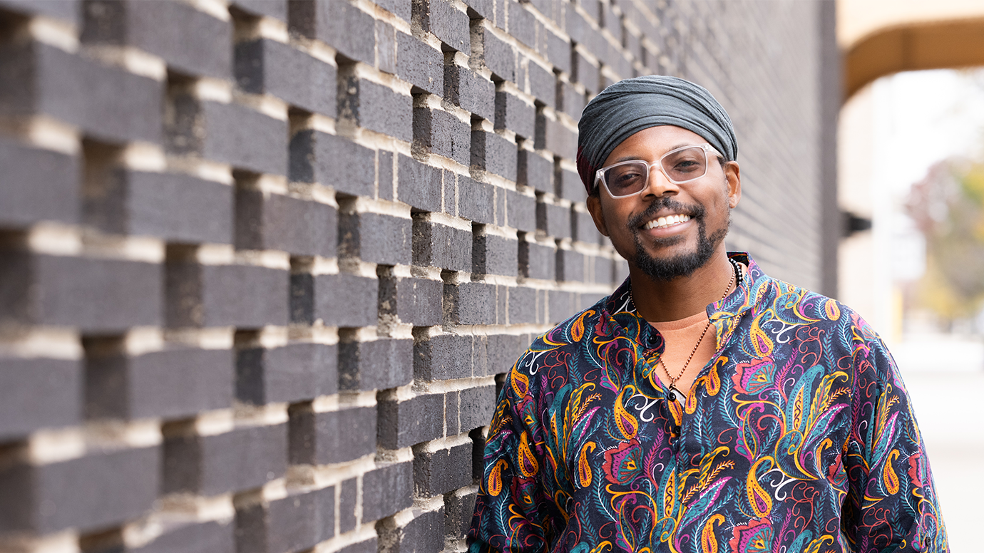 Justin D. Williams smiles in front the brick wall of the Green Line Performing Arts Center. Part of the elevated tracks of the CTA are visible.