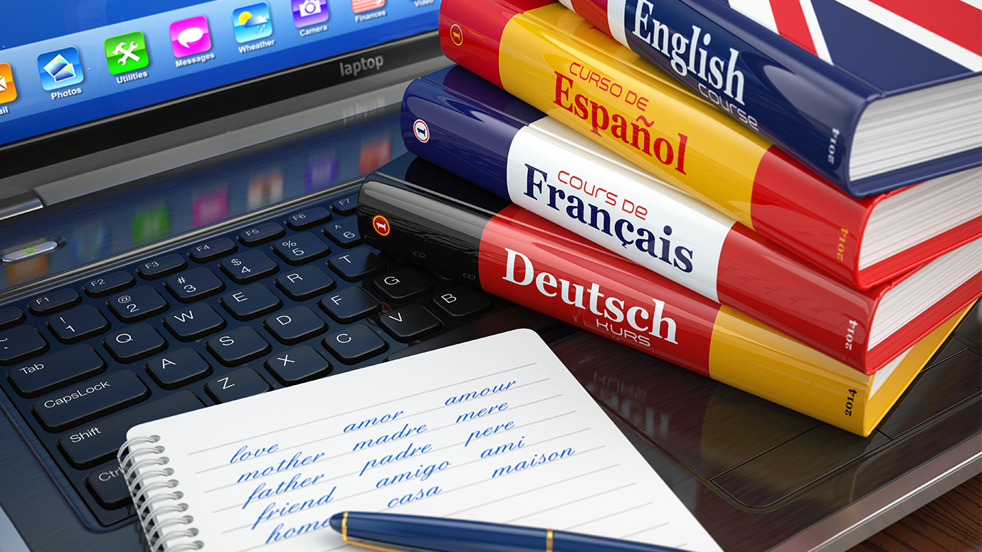 A stack of German, French, Spanish and English language books sits on a laptop keyboard next to a notebook and pen. Written on the notebook are translations for "love," "mother," "father," "family" and "home" in several languages.