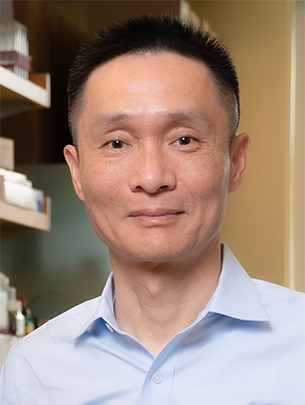 Photo of Chuan He looking at camera against a backdrop of a lab