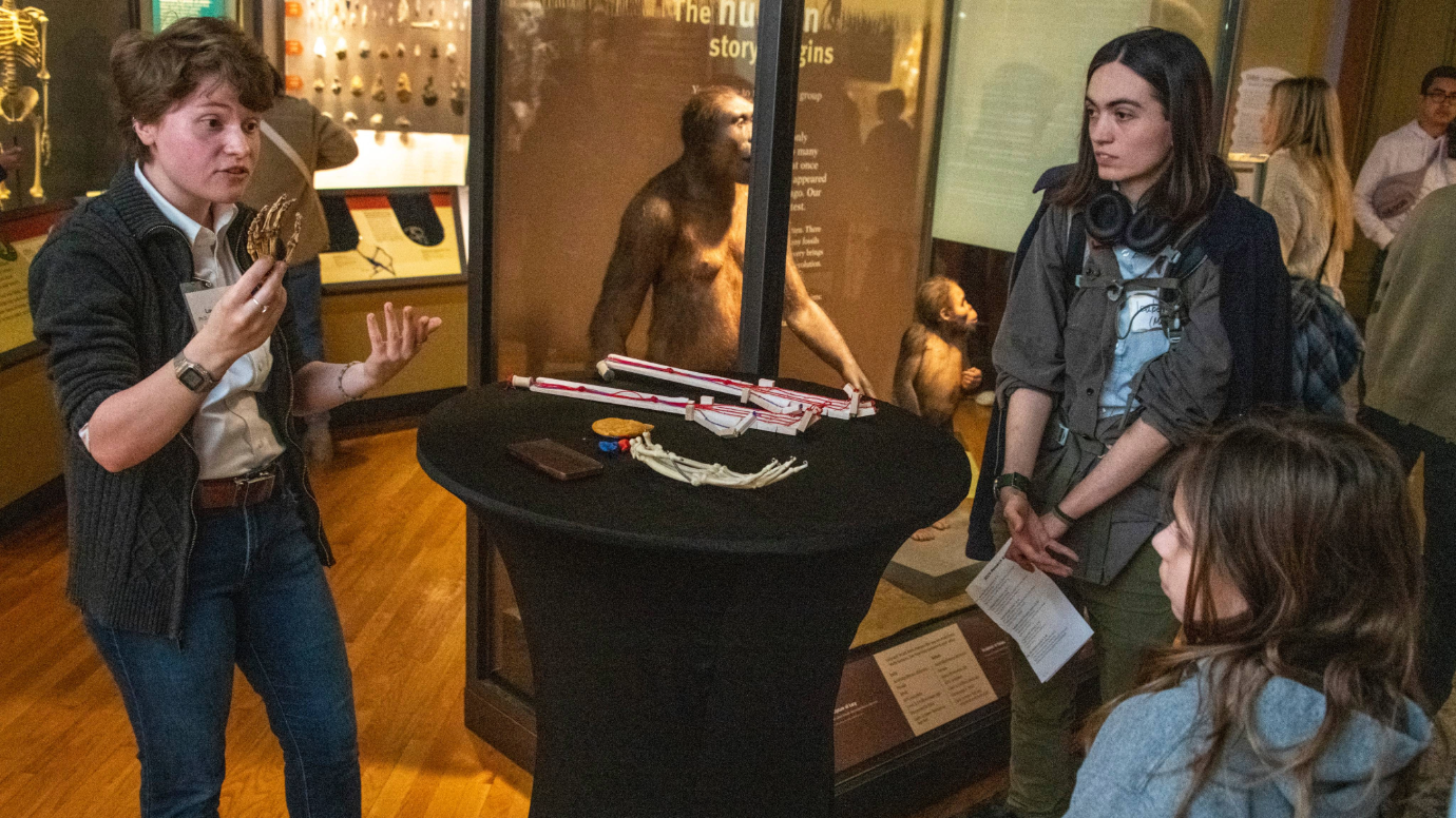 Laura Hunter speaks to a group of museum visitors in front of a museum display case featuring hominid Lucy.