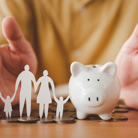 A piggy bank and paper cutout of a family with hands blocking the sides