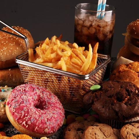 A table with burgers, soda, french fries, doughnuts, and other unhealthy foods