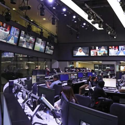 A room lined with a dozen televisions in which several journalists are working