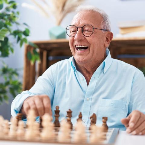 A senior citizen smiles and plays chess