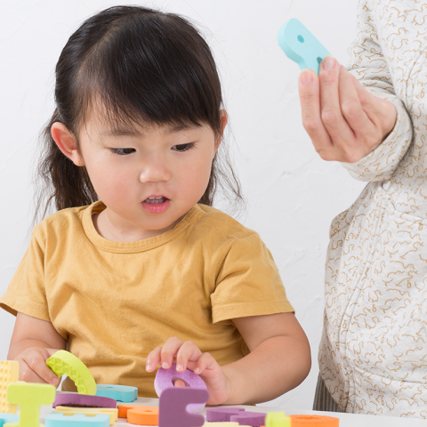 A young child plays with letter blocks while an adult watches on. 