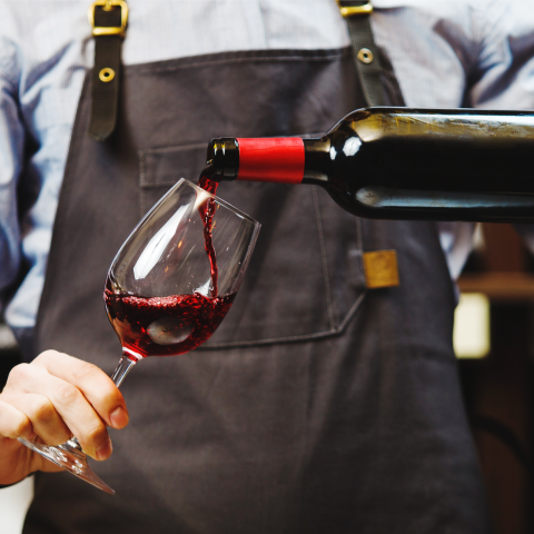 A bartender pours a glass of red wine