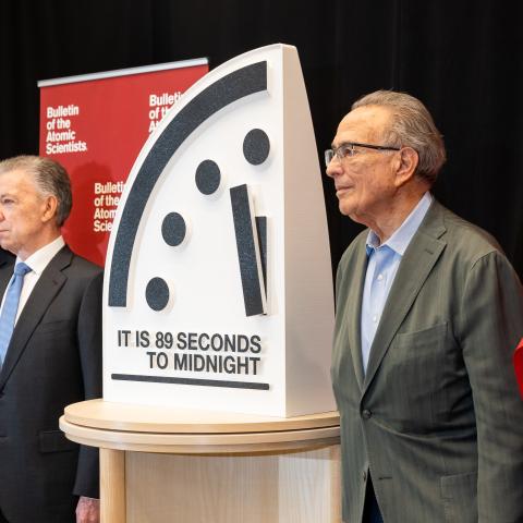 Photo of five people in suits standing at a press conference around a clock reading "89 seconds to midnight".