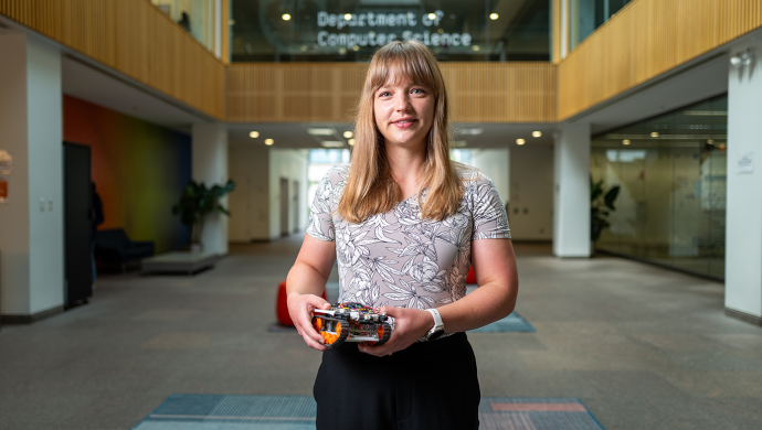 Sarah Sebo stands in the lobby of the Department of Computer Science holding a small tank-like robot