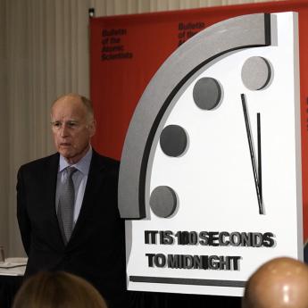 Three people stand at the newly unveiled Doomsday Clock