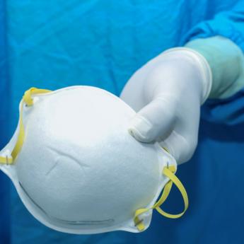 Gowned and gloved surgeon holds a discarded N95 mask