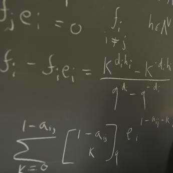 A hand writes mathematical equations on a chalkboard.
