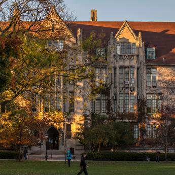 People walk past Eckhart Hall on the campus of the University of Chicago with trees turning colors.
