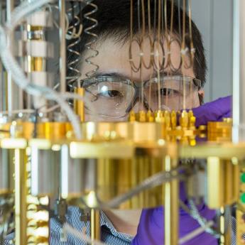 Scientist Dafei Jin working with gloves and goggles on an array of brass tubes