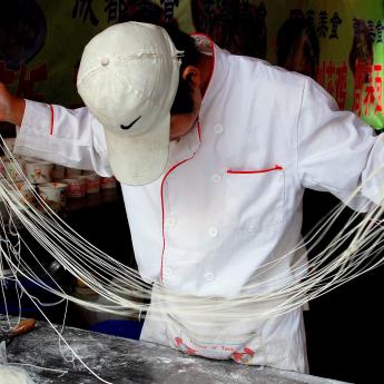 Restaurant worker holds long strands of hand-pulled noodles