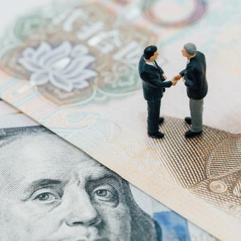 Toy men shake hands, standing on cash bills from the United States and China