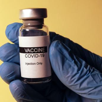 COVID-19 vaccine vial held by a hand in blue rubber gloves