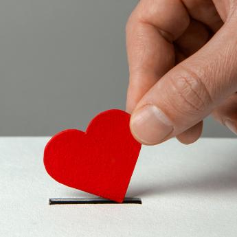 A hand holding a paper heart, inserting it into a coin slot