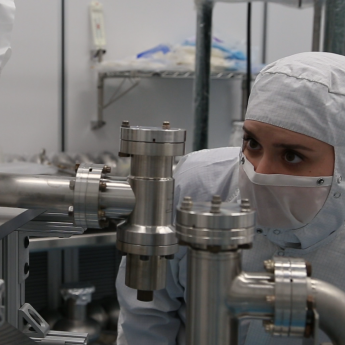 Person in gown and face covering works on metal technological components