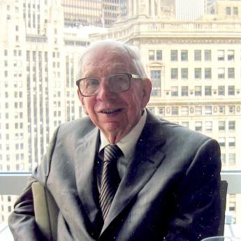 George S. Tolley sits in front of a window, with Chicago buildings in the background