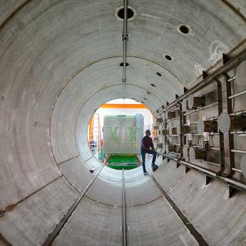Worker stands in a huge tunnel as MIcroBooNE equipment is loaded