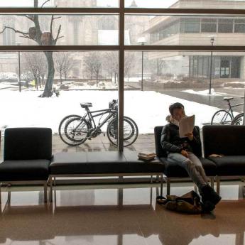 A student sits inside on a snowy day reading a book