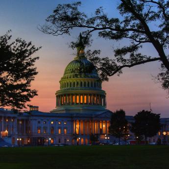 A view of the U.S. Capitol building at sunset, with trees in the foreground
