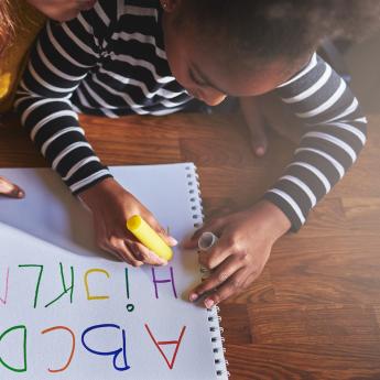 A pre-K student practices writing ABCs with an adult