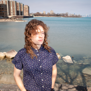 Chaillé Biddle stands on the shore of Lake Michigan on clear day with buildings visible