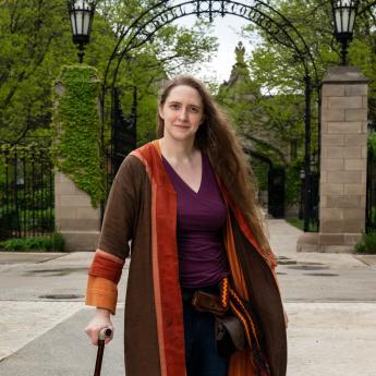 UChicago historian Ada Palmer stands with a cane on campus in front of Hull Gate Gate