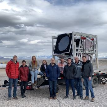 A group of scientists outdoors in front of a large square metal apparatus