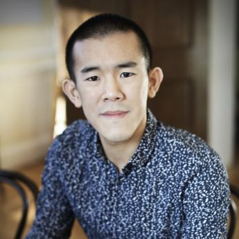 Portrait of Ed Yong looking at camera wearing speckled button-down shirt