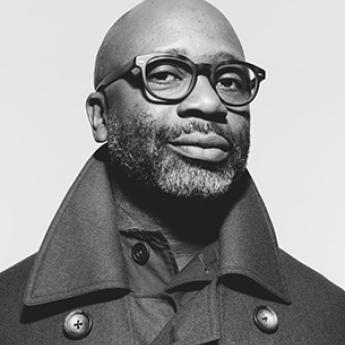 Black and white portrait of Theaster Gates looking at camera in coat