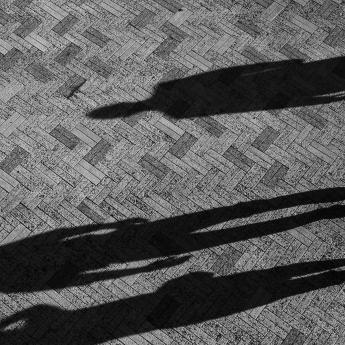 Birds-eye view of three figures in silhouette walking across pavement, casting long shadows