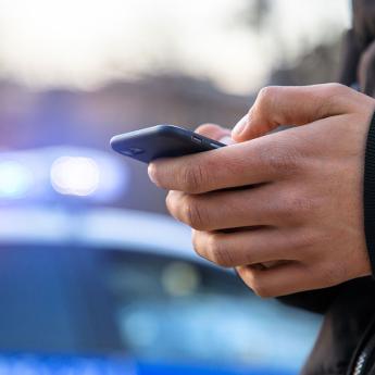 A person scrolls through social media while standing near a police car