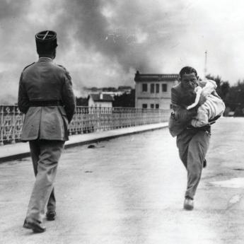 A man carries a baby to safety across a bridge connecting Spain and France during the 1936 Battle of Irun in the Spanish Civil War