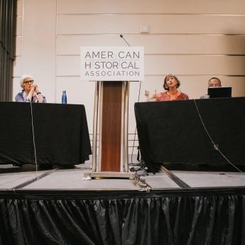 Five panel members sit behind a podium labeled "American Historical Association"
