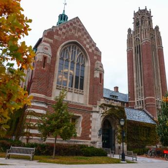 A brick building with glass facade stands next to a bell tower