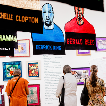 Visitors look at a gallery wall filled with poetry and framed artwork. Quilted portraits of Abdul Muhammad, Michelle Clopton, Derrick King, Gerald Reed and Robert Allen hang in the foreground.  
