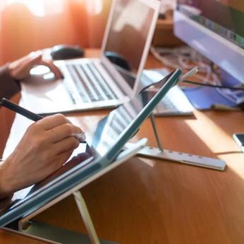 A person writes with a pen while working at a computer